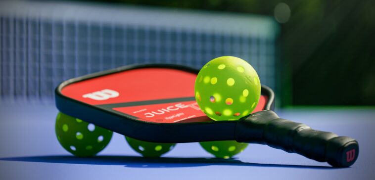 Raquete de pickleball com bolas perfuradas no chão de uma quadra